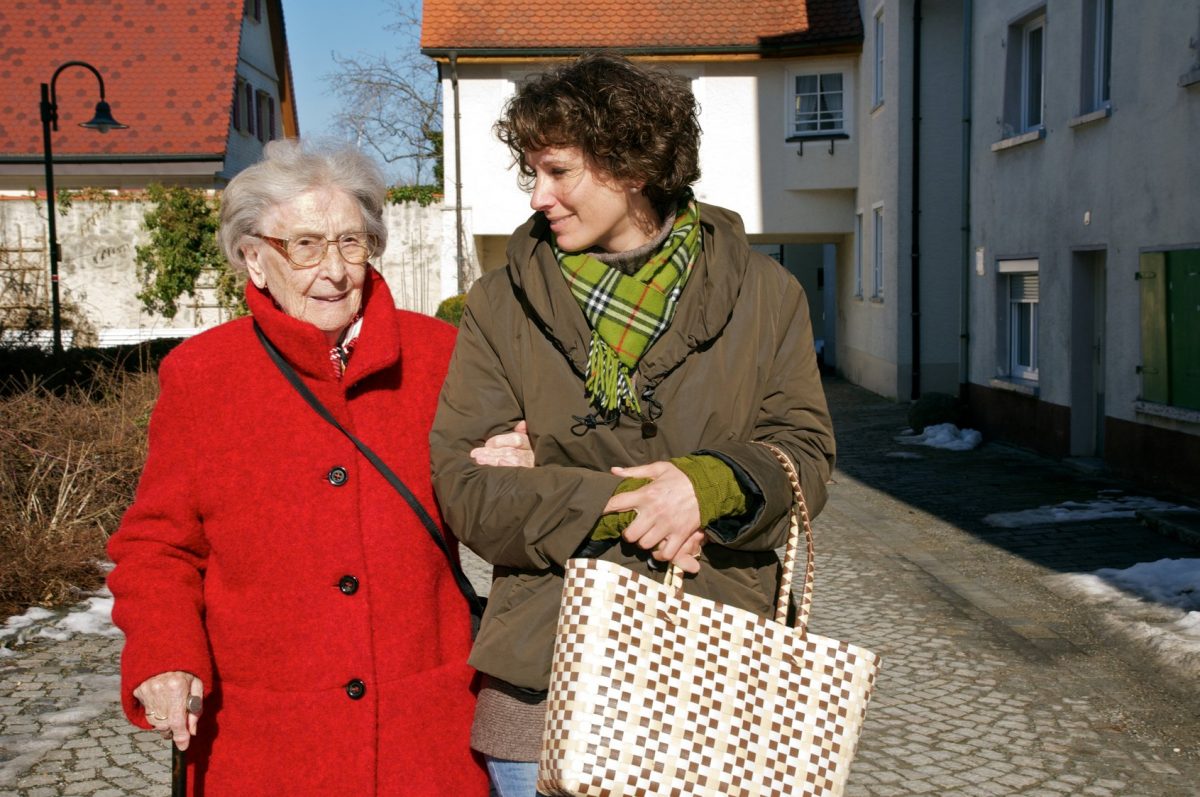 Eine Seniorin wird von einer jüngeren Frau beim Spazieren begleitet