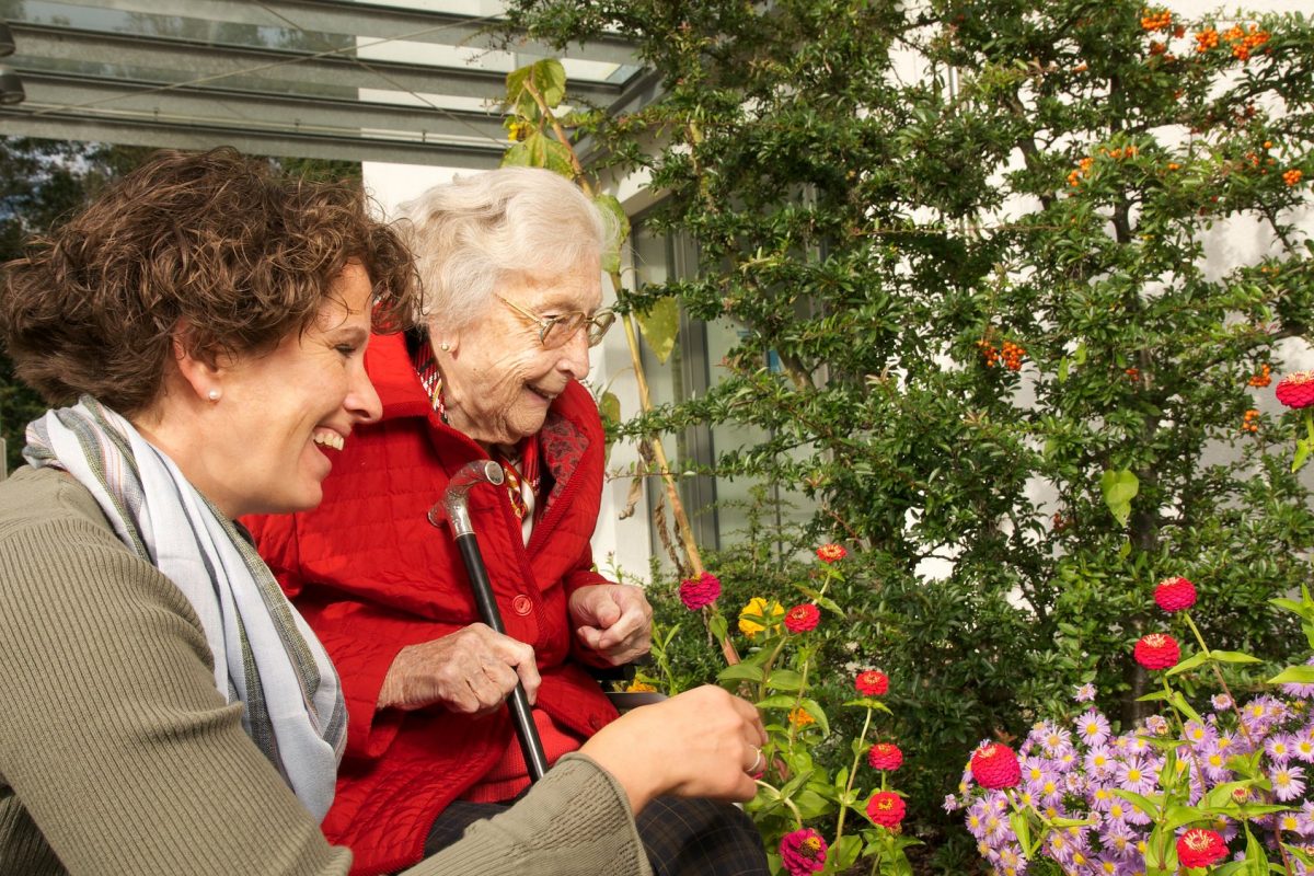 Eine Seniorin und eine jüngere Frau schauen sich die Blumen im Garten an