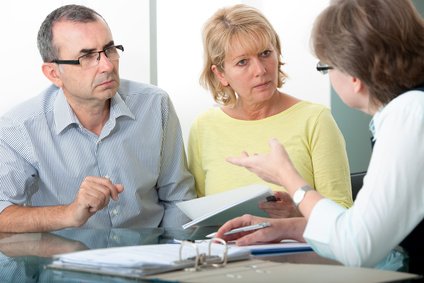 Eine Seniorin im Sessel wird von einer Frau von hinten umarmt