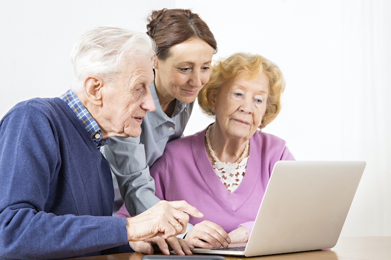 Eine Seniorin im Sessel wird von einer Frau von hinten umarmt