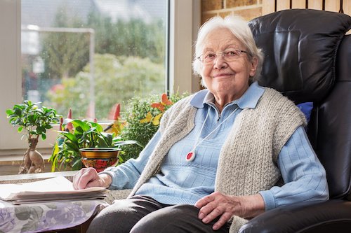 Eine Seniorin sicher im Sessel mit Ihrem Hausnotruf Knopf.