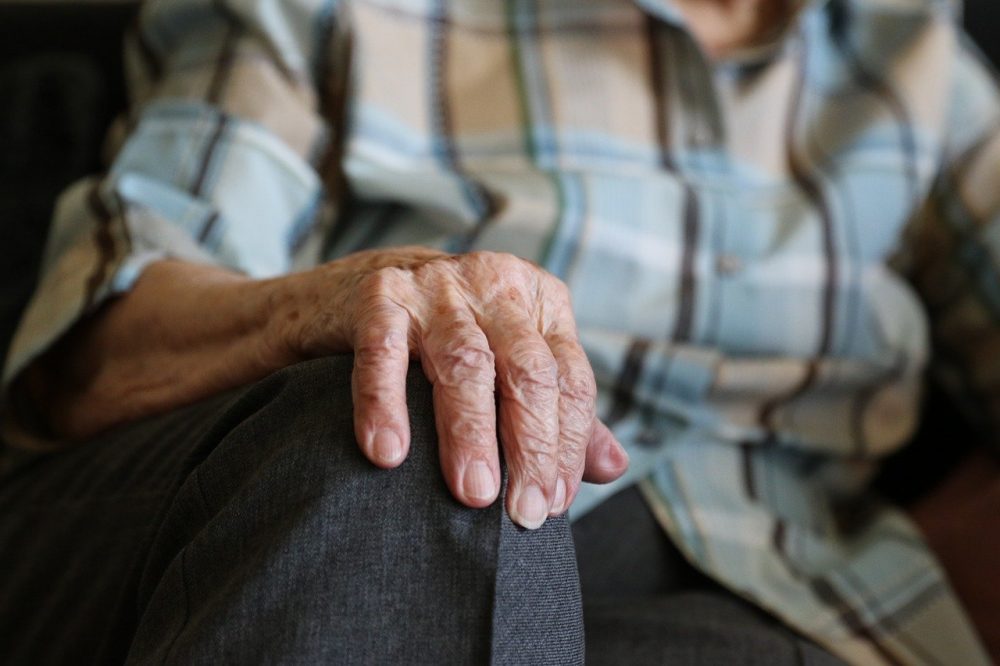 Eine Seniorin im Sessel wird von einer Frau von hinten umarmt