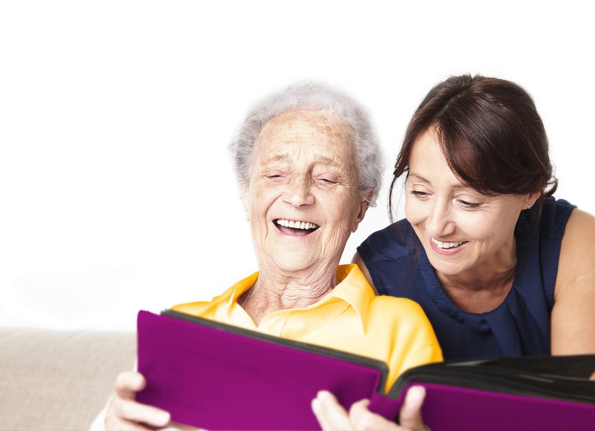 Eine Seniorin im Sessel wird von einer Frau von hinten umarmt