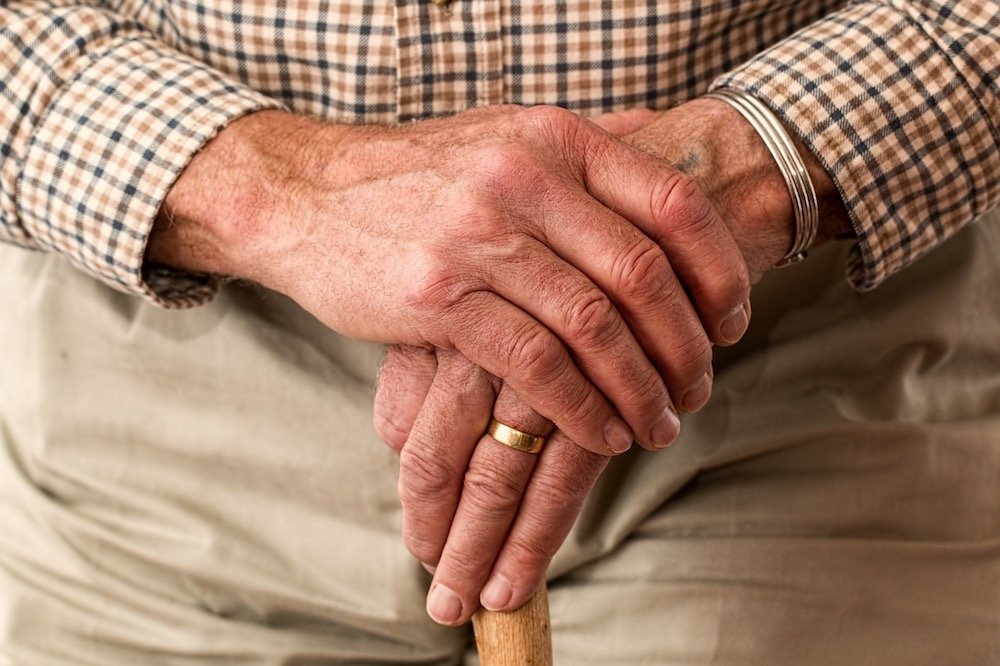Eine Seniorin im Sessel wird von einer Frau von hinten umarmt