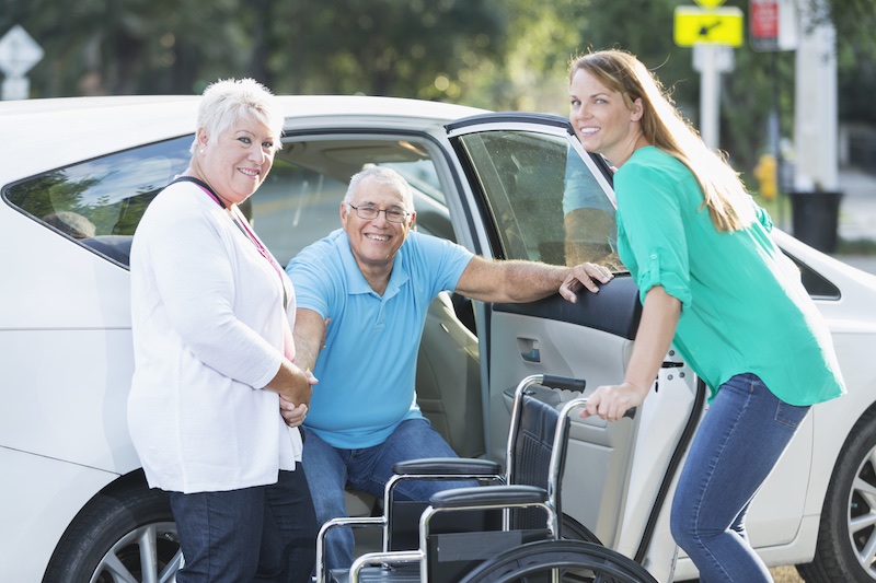 Eine Seniorin im Sessel wird von einer Frau von hinten umarmt